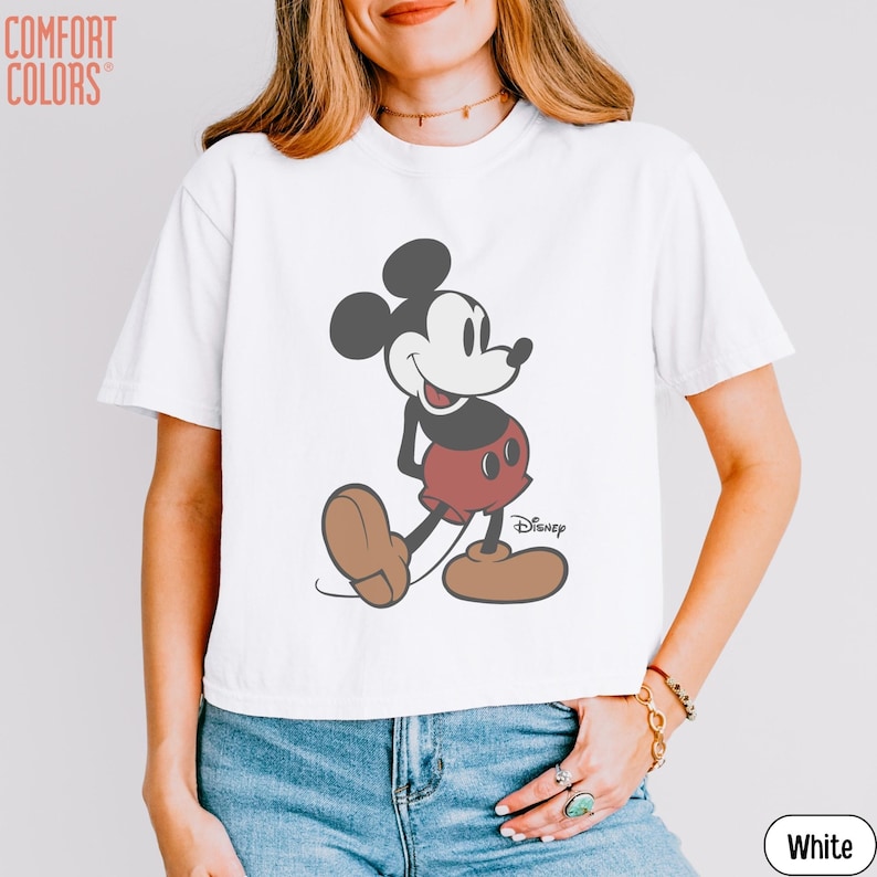May include: White t-shirt featuring a classic Mickey Mouse graphic. The cartoon character is depicted in black, red, and brown, with the Disney logo. The shirt is a Comfort Colors brand.
