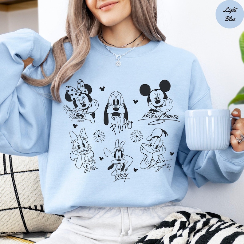 May include: Light blue sweatshirt featuring black and white illustrations of Disney characters, including Mickey Mouse, Minnie Mouse, Pluto, Daisy Duck, Goofy, and Donald Duck. The text "Light Blue" is in a circle in the upper right corner.
