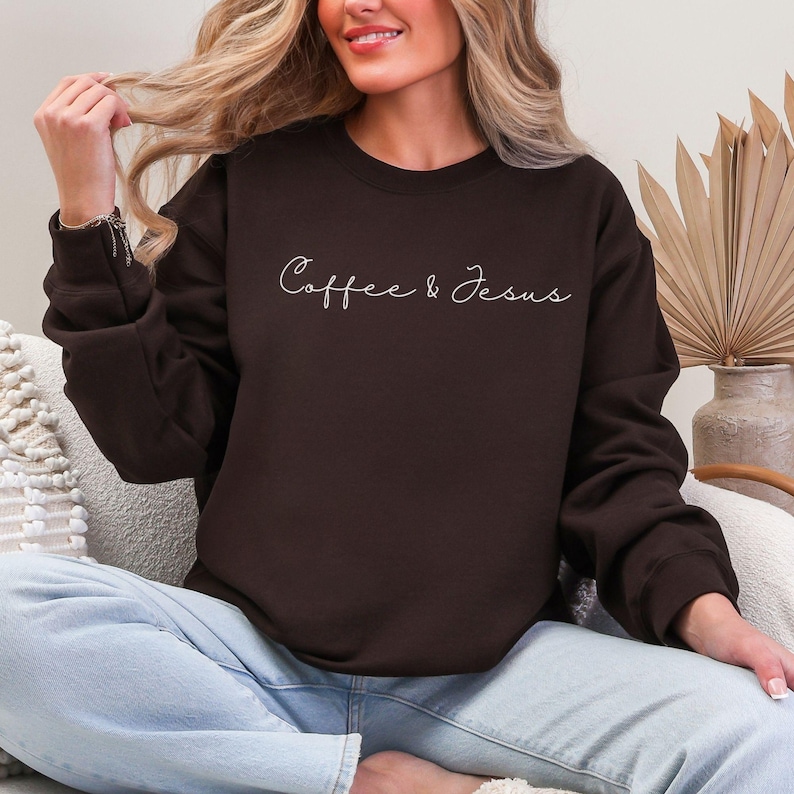 Puede incluir: Una sudadera marr&oacute;n oscuro con la inscripci&oacute;n "Coffee & Jesus" en escritura blanca. La parte superior de manga larga con cuello redondo est&aacute; hecha de un material suave. La sudadera es de estilo casual.