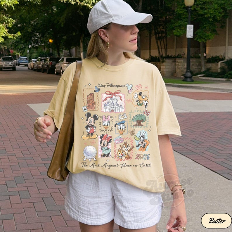 K&ouml;nnte beinhalten: Hellgelbes T-Shirt mit einem Disney-Motiv. Das Design zeigt Micky Maus, Minnie Maus und andere Charaktere sowie den Text "Walt Disneyland" und "The Most Magical Place on Earth".