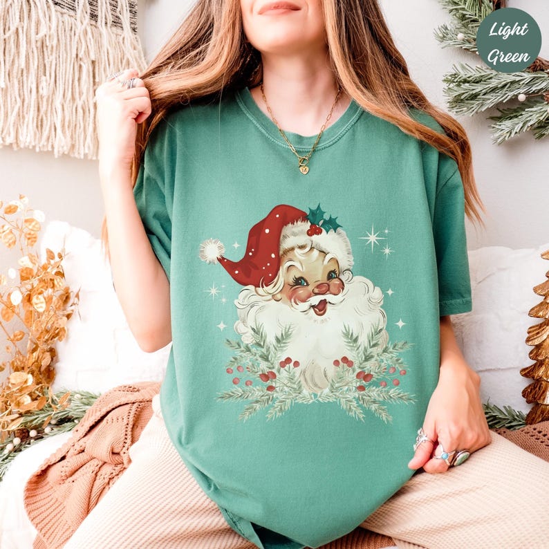 May include: A light green t-shirt featuring a vintage Santa Claus graphic. The Santa Claus illustration has a red hat, white beard, and is surrounded by greenery and berries. The text "Light Green" is in the upper right corner.