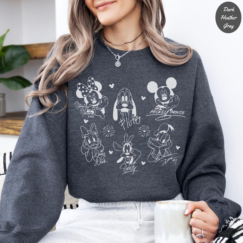 May include: A white ceramic mug with a black handle and the text "But First, Coffee" in a bold, black font. The mug is set against a blurred background, highlighting its clean design.