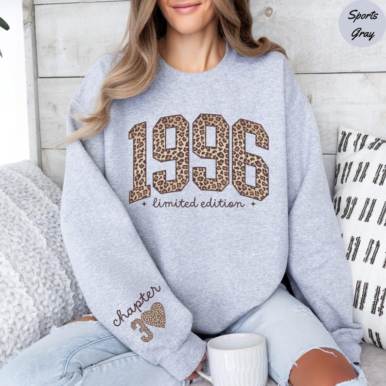Op de afbeelding: Een lichtgrijs sweatshirt met het jaar "1996" in een luipaardprint ontwerp. De tekst "limited edition" staat onder het jaar. De linkermouw heeft de tekst "chapter 39" met een luipaardprint hart.
