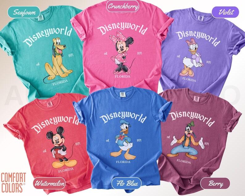 May include: A collection of Comfort Colors t-shirts in various colors, each featuring a Disney World graphic. The shirts display different Disney characters, including Mickey Mouse, Minnie Mouse, Donald Duck, Pluto, Daisy Duck, and Goofy. The text "Disneyworld" and "Florida" are printed on each shirt.