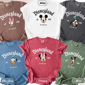 May include: A collection of six Comfort Colors t-shirts in various colors, including white, espresso, and blue jean. Each shirt features the Disneyland logo with a character graphic and the text "PARIS" and "1992".