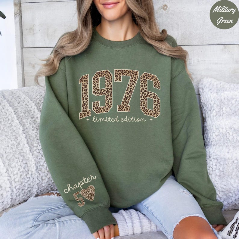 Op de afbeelding: Militairgroen sweatshirt met het jaar "1976" in een luipaardprint ontwerp. De woorden "limited edition" staan onder het jaar. De linkermouw heeft de woorden "chapter 50" en een luipaardprint hart.