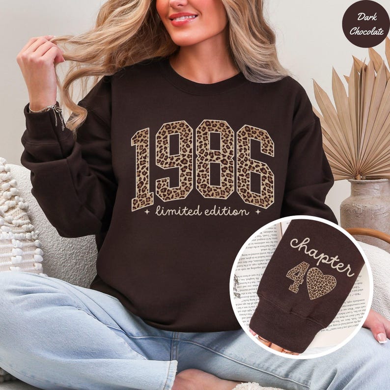 Op de afbeelding: Donker chocoladebruine sweatshirt met het jaartal "1986" in een luipaardprint ontwerp. De woorden "limited edition" staan eronder. Een kleinere afbeelding toont een bruine mouw met het woord "chapter" en het nummer "40" met een luipaardprint hart.