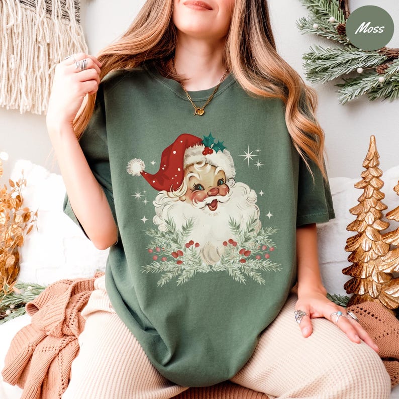 May include: Olive green t-shirt featuring a vintage Santa Claus graphic. The Santa Claus illustration has a red hat, white beard, and is surrounded by a wreath of greenery and berries. The shirt is a comfortable, casual style.