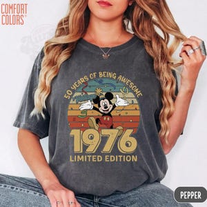 Puede incluir: Camiseta gris oscuro Comfort Colors con un dise&ntilde;o vintage de Mickey Mouse. El dise&ntilde;o incluye a Mickey Mouse, el a&ntilde;o 1976 y las palabras "50 Years of Being Awesome" y "Limited Edition."