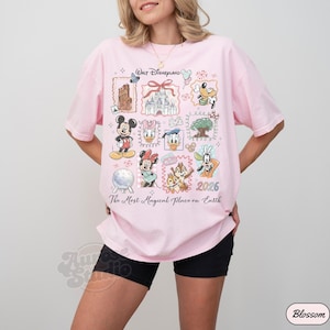 K&ouml;nnte beinhalten: Ein hellrosa T-Shirt mit einem Disney-Motiv. Das Design zeigt verschiedene Disney-Charaktere und Wahrzeichen mit dem Text "Walt Disneyland" und "The Most Magical Place on Earth".