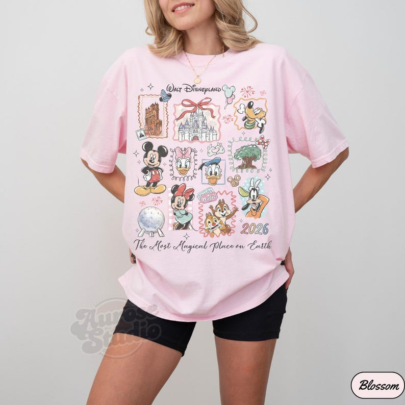 K&ouml;nnte beinhalten: Ein hellrosa T-Shirt mit einem Disney-Motiv. Das Design zeigt verschiedene Disney-Charaktere und Wahrzeichen mit dem Text "Walt Disneyland" und "The Most Magical Place on Earth".
