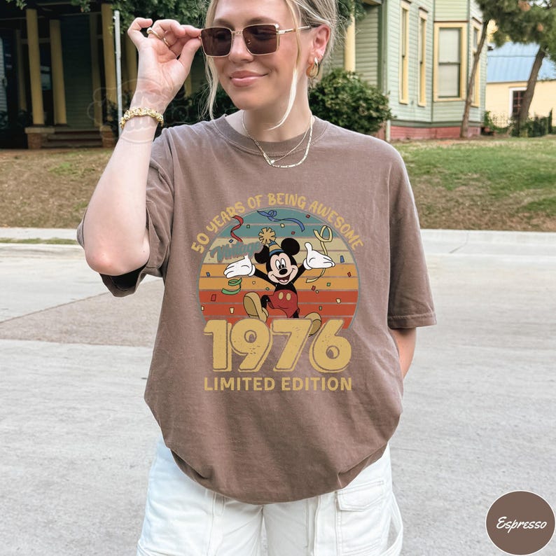Puede incluir: Camiseta marr&oacute;n con un dise&ntilde;o retro de Mickey Mouse, el texto "50 YEARS OF BEING AWESOME 1976 LIMITED EDITION". El dise&ntilde;o utiliza una paleta de colores vintage de naranja, amarillo y marr&oacute;n.