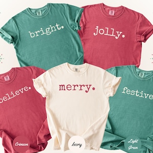 Puede incluir: Cinco camisetas de manga corta y cuello redondo en color carmesí, marfil y verde claro. Las camisetas presentan texto en blanco o rojo impreso en la parte delantera con las palabras bright, jolly, believe, merry y festive, cada una con un punto.