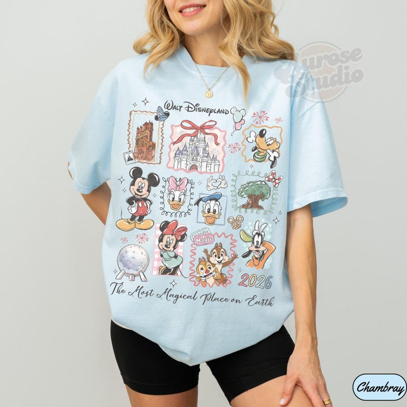 K&ouml;nnte beinhalten: Hellblaues T-Shirt mit Disney-Motiven. Es zeigt Micky Maus, Donald Duck und weitere Charaktere. Der Text beinhaltet "Walt Disneyland" und "The Most Magical Place on Earth 2026". Das Design ist von Rahmen umgeben.