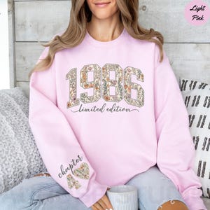 May include: Light pink sweatshirt with the year "1986" in a floral design. The words "limited edition" are below the numbers. The left sleeve has the word "chapter" and a floral heart with the number "4".