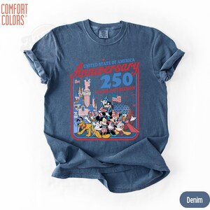 May include: Denim blue t-shirt featuring a graphic celebrating the United States of America's 250th Anniversary. The graphic includes Disney characters, a castle, and the text "United State of America Anniversary 250 Years of Freedom."