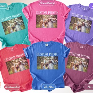 K&ouml;nnte beinhalten: Eine Auswahl an Comfort Colors T-Shirts in verschiedenen Farben, darunter Seegr&uuml;n, Pink, Lila, Rot, Blau und Beere. Jedes Shirt zeigt einen individuellen Fotodruck mit dem wei&szlig;en Text "CUSTOM PHOTO".