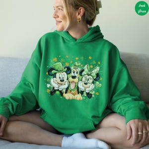 May include: Green hoodie featuring Mickey Mouse, Pluto, and Minnie Mouse in St. Patrick's Day attire. Mickey wears a green hat, Pluto has a green collar, and Minnie has a green bow and glasses. The design includes shamrocks and the words "Lucky You".