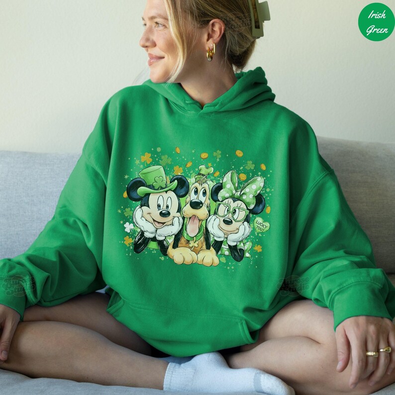 May include: Green hoodie featuring Mickey Mouse, Pluto, and Minnie Mouse in St. Patrick's Day attire. Mickey wears a green hat, Pluto has a green collar, and Minnie has a green bow and glasses. The design includes shamrocks and the words "Lucky You".