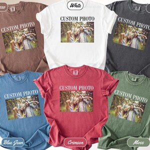 K&ouml;nnte beinhalten: Eine Auswahl an Comfort Colors T-Shirts in verschiedenen Farben, darunter Espresso, Wei&szlig;, Pfeffer, Blue Jean, Karmesinrot und Moos. Jedes Shirt zeigt ein gedrucktes Foto und den Text "CUSTOM PHOTO". Die &Auml;rmel sind hochgekrempelt.