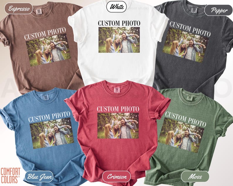 K&ouml;nnte beinhalten: Eine Auswahl an Comfort Colors T-Shirts in verschiedenen Farben, darunter Espresso, Wei&szlig;, Pfeffer, Blue Jean, Karmesinrot und Moos. Jedes Shirt zeigt ein gedrucktes Foto und den Text "CUSTOM PHOTO". Die &Auml;rmel sind hochgekrempelt.