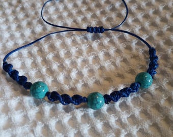 Puede incluir: Una pulsera de macramé azul con tres cuentas de color turquesa. La pulsera es ajustable con un cierre de nudo corredizo. El cordón de macramé es azul oscuro y las cuentas tienen un aspecto moteado. Diseño sencillo.