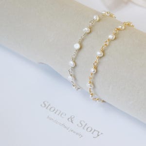 May include: Two delicate bracelets with freshwater pearls. One bracelet is silver-toned, the other is gold-toned. The bracelets are displayed on a light-colored surface. The image also shows the text "Stone & Story, handcrafted jewelry."