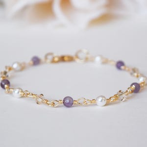 May include: A delicate gold bracelet featuring alternating purple, white, and clear beads. The bracelet is strung on a gold chain and has a gold clasp. The beads are round and smooth, creating an elegant and refined look.