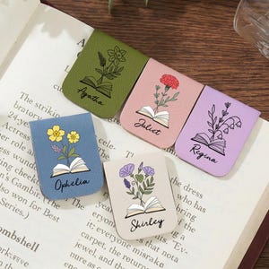 May include: Five leather bookmarks with floral designs and names: Agatha, Juliet, Ophelia, Regina, and Shirley. The bookmarks are in various colours and are placed on an open book.