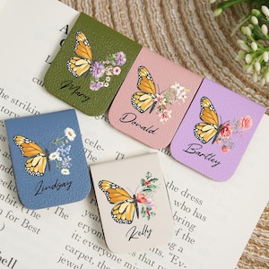 Puede incluir: Conjunto de marcapáginas de cuero personalizados, cada uno con un diseño de mariposa monarca y detalles florales. Los colores incluyen verde, rosa y azul. Nombres como Mary, Donald, Bartley, Lindsay y Kelly están impresos.