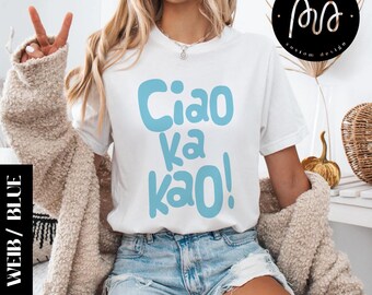 May include: White t-shirt with the phrase "Ciao ka kao!" in light blue. The shirt is worn with denim shorts and a beige cardigan. A black and white rectangle with the words "WEIB / BLUE" is on the left side of the image.