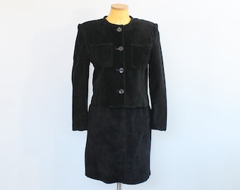 May include: A black corduroy skirt suit with a button-up jacket. The jacket has two flap pockets and the skirt is knee-length.
