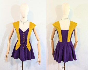 May include: A purple and gold mini dress with a fitted bodice and a flared skirt. The dress has a V-neckline and a button closure at the front.