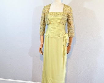 May include: A pale yellow formal dress with a matching bolero jacket. The dress has a square neckline and a gathered bodice. The bolero is embellished with gold sequins. The dress is displayed on a mannequin.