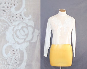 May include: White cotton blouse with a high neck and long sleeves. The blouse features delicate white embroidery of roses and leaves.