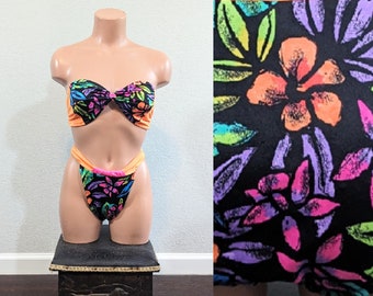 May include: A black and orange bikini with a tropical floral print. The top is a bandeau style and the bottom is a high-cut style.