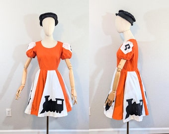 May include: A vintage orange and white dress with a black train silhouette and musical note on the bodice. The dress has a full skirt and short puff sleeves.