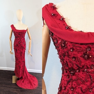 Puede incluir: Un vestido de noche largo, rojo, con cuentas, con un escote de un solo hombro y una cola fluida.