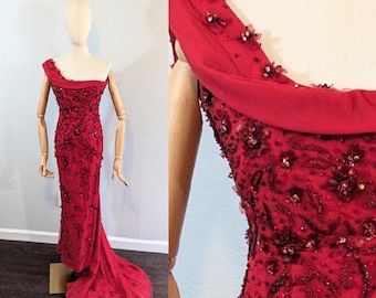 May include: A long, red, beaded evening gown with a one-shoulder neckline and a flowing train.