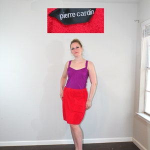 May include: A woman wearing a purple tank top and a red skirt. The skirt has a pocket on the front. The image also shows a red towel with the text "pierre cardin" on a black label.