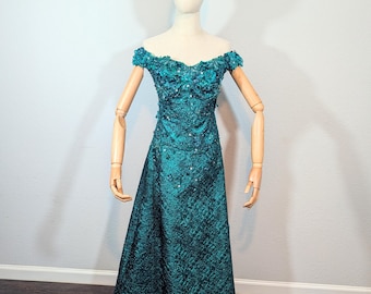 May include: A teal off-the-shoulder formal gown with floral embellishments and a scattering of sequins. The dress is displayed on a mannequin and features a full skirt. A silver tiara sits atop the mannequin's head.