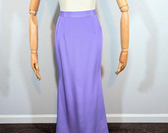 May include: A lilac-colored, floor-length skirt displayed on a mannequin. The skirt has a fitted waist and a slight flare towards the hem. The fabric appears smooth and has a subtle sheen. The mannequin is set against a neutral background.