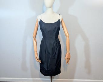 May include: A black, knee-length slip dress with thin spaghetti straps. The dress is displayed on a mannequin with wooden arms and a cream-colored head. The mannequin is mounted on a gold-colored metal stand.