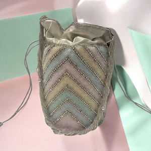 May include: A beaded drawstring bag with a chevron pattern in pastel colors. The bag features silver-colored beads and a satin lining. The bag's design includes a mix of light blue, pink, and yellow hues.