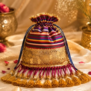 May include: A drawstring pouch featuring horizontal stripes in red, blue, yellow, and green. The lower section is adorned with a wide band of intricate gold lace. The bag is finished with a series of magenta cords ending in gold-colored tassels.