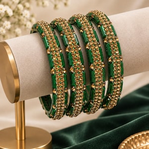May include: A set of four circular bangles featuring a vibrant green base accented with a central band of small, sparkling amber-colored crystals. Each bangle has a smooth, polished finish and a consistent width, creating a uniform appearance.