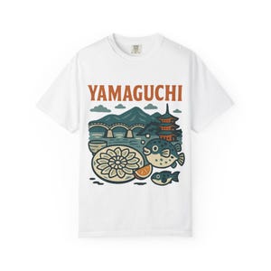 May include: White t-shirt with a graphic design featuring a Japanese pagoda, a bridge, a mountain, a pufferfish, and a plate of food. The text "YAMAGUCHI" is printed in orange on the shirt.
