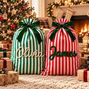 Può includere: Due grandi sacchi regalo in tessuto a righe verticali, uno verde e bianco con il nome Olivia in corsivo bianco, e uno rosso e bianco con il nome James in corsivo verde. Ogni sacco è chiuso nella parte superiore da un fiocco in velluto verde.