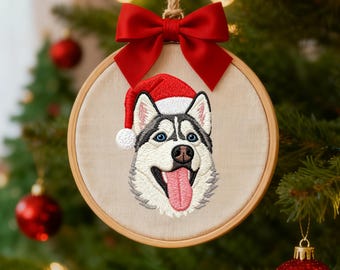 May include: Embroidered Christmas ornament featuring a Siberian Husky wearing a Santa hat. The dog has blue eyes, a pink tongue, and a black and white coat. The ornament is round, framed in wood, and adorned with a red bow and hanging string.