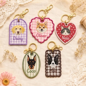 Pode incluir: Cinco porta-chaves bordados com fechos de mosquetão dourados. Cada um apresenta o retrato de um animal e um nome: Daisy num arco de xadrez roxo, Oliver num coração de xadrez rosa, Nala num coração vermelho com pontos brancos, Coco num oval e Milo num retângulo de xadrez castanho.